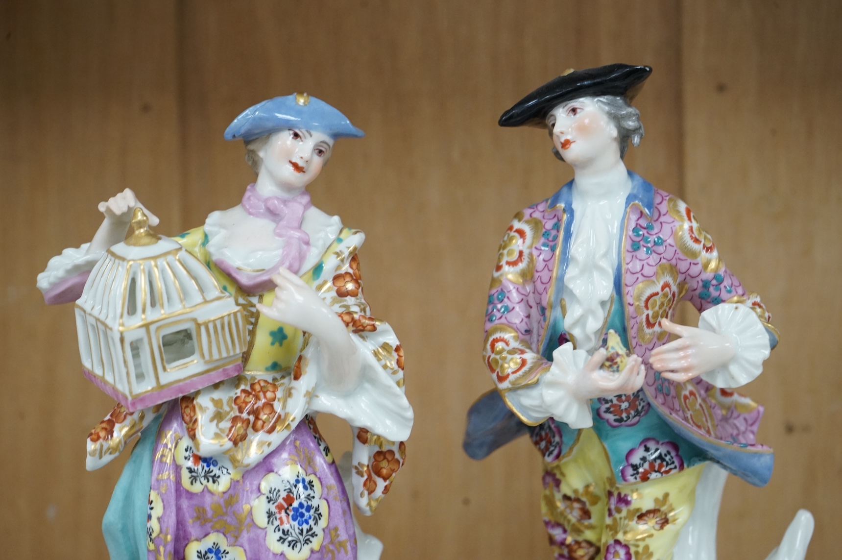 A pair of Derby style figures of a lady holding a bird cage and a gentleman holding a bird, tallest 23cm high